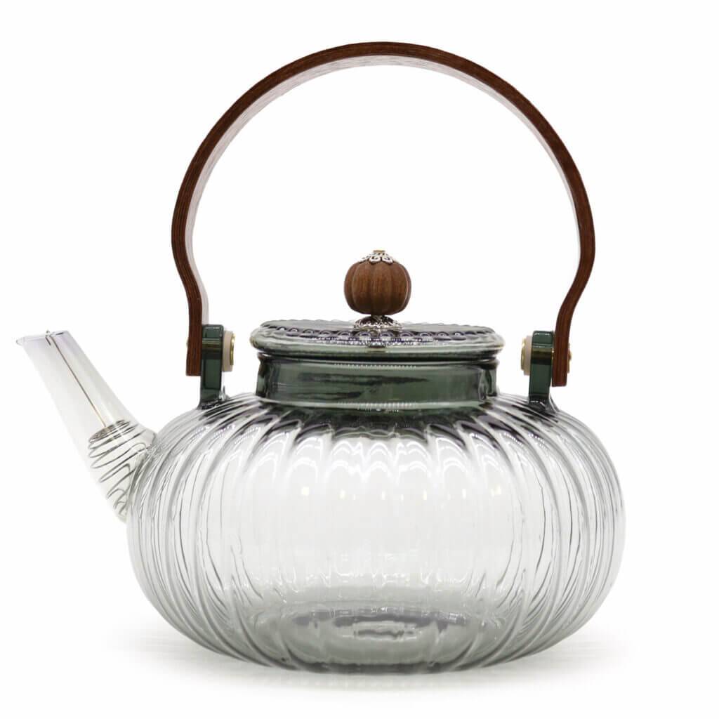 Clear glass teapot with a ribbed design, short spout, metal lid topped with a wood knob, and a curved wooden handle.