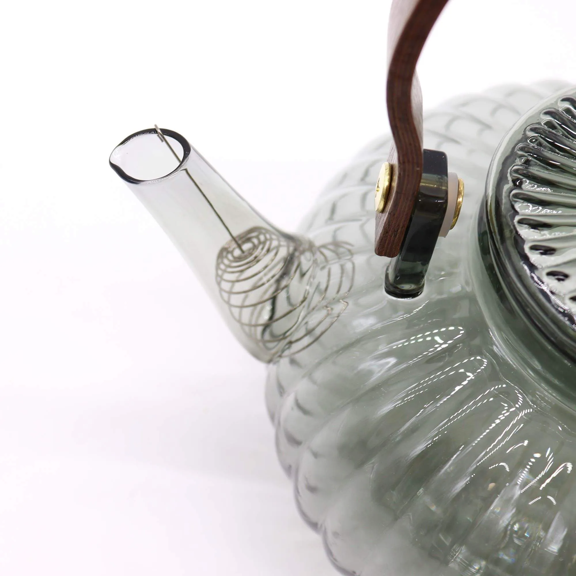 Close-up of a transparent glass teapot with a ribbed design, wooden handle, and a visible metal filter inside the spout.