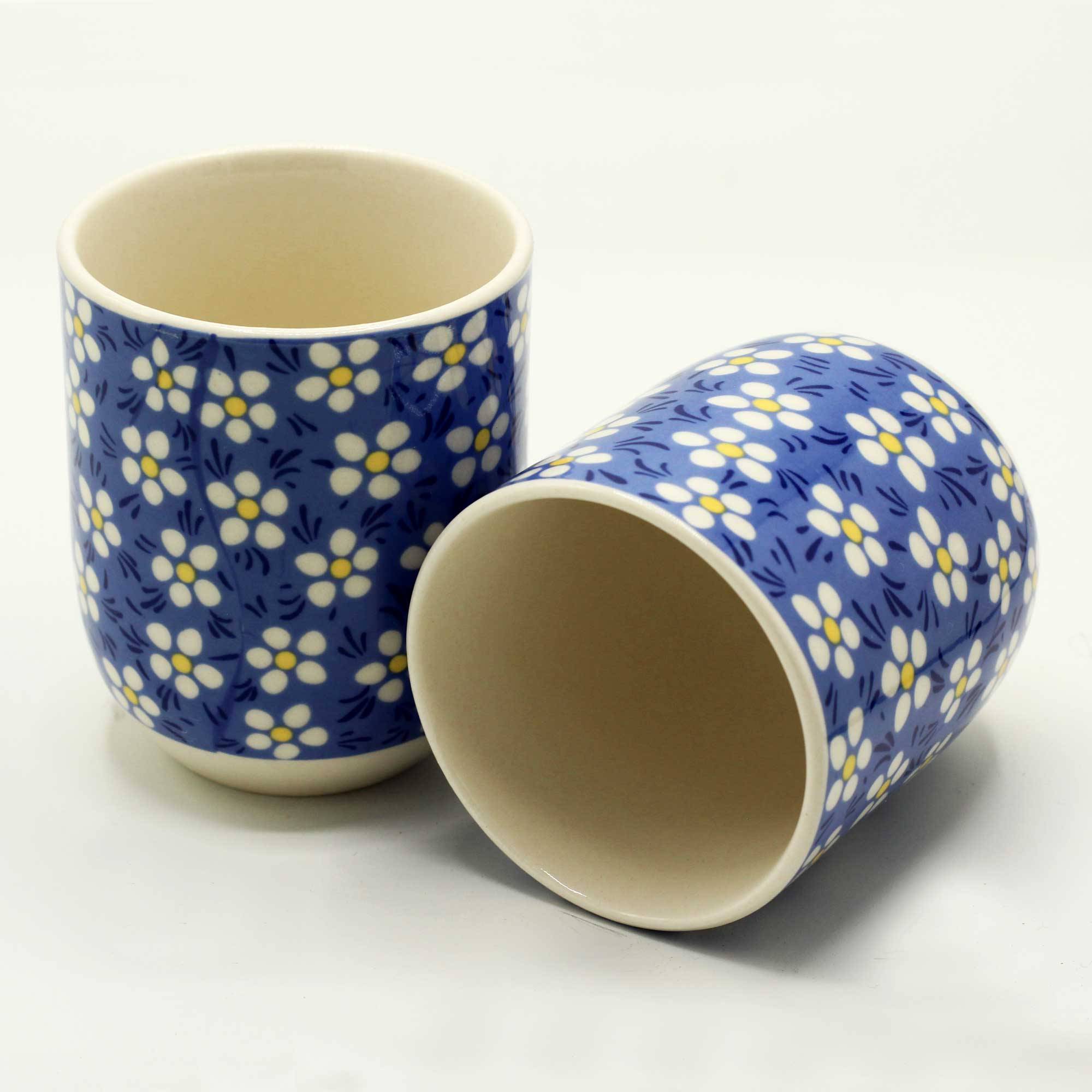 Two ceramic cups with a blue background and white floral pattern, one standing upright and the other lying on its side, on a plain white surface.