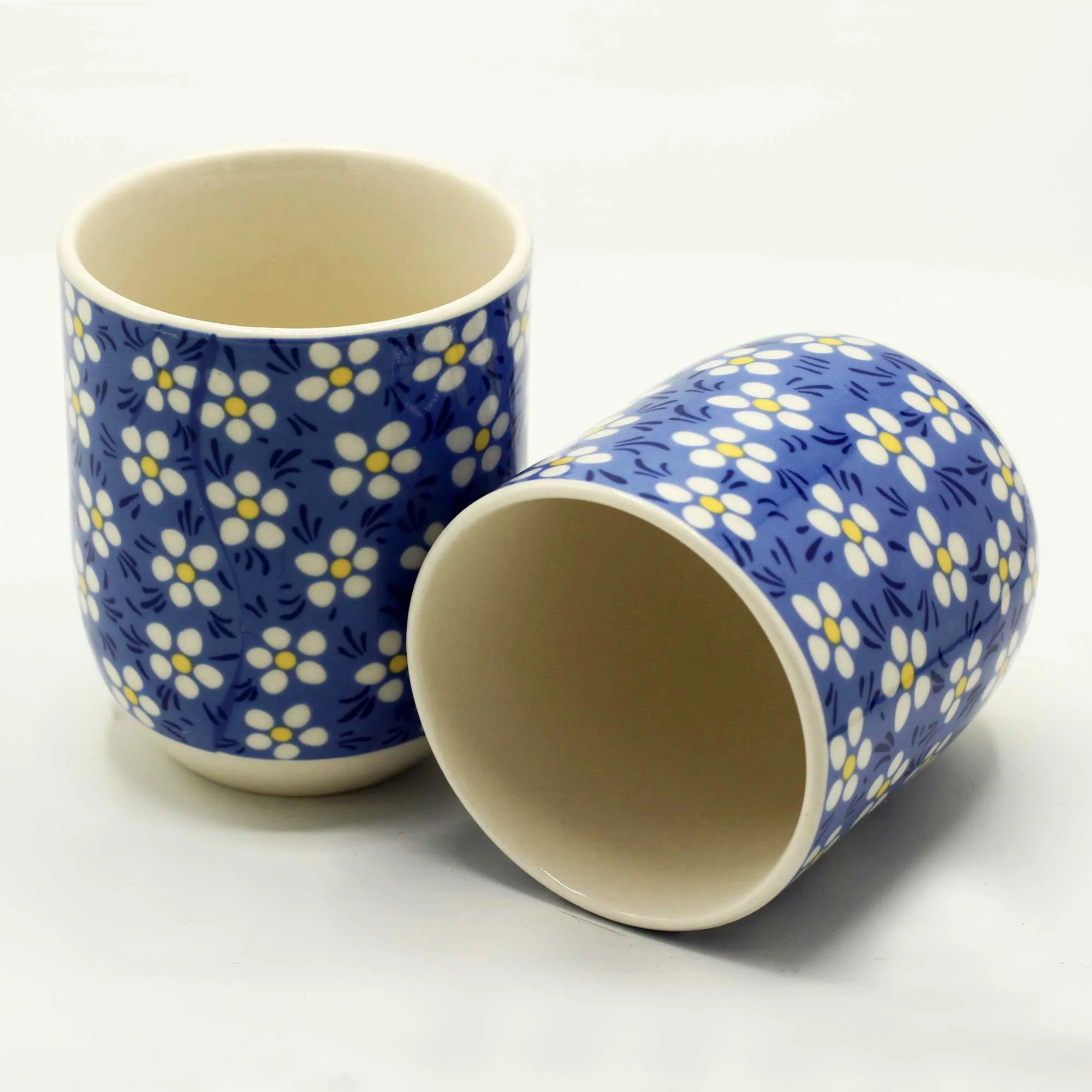 Two ceramic cups with a blue background and white floral pattern, one standing upright and the other lying on its side, on a plain white surface.