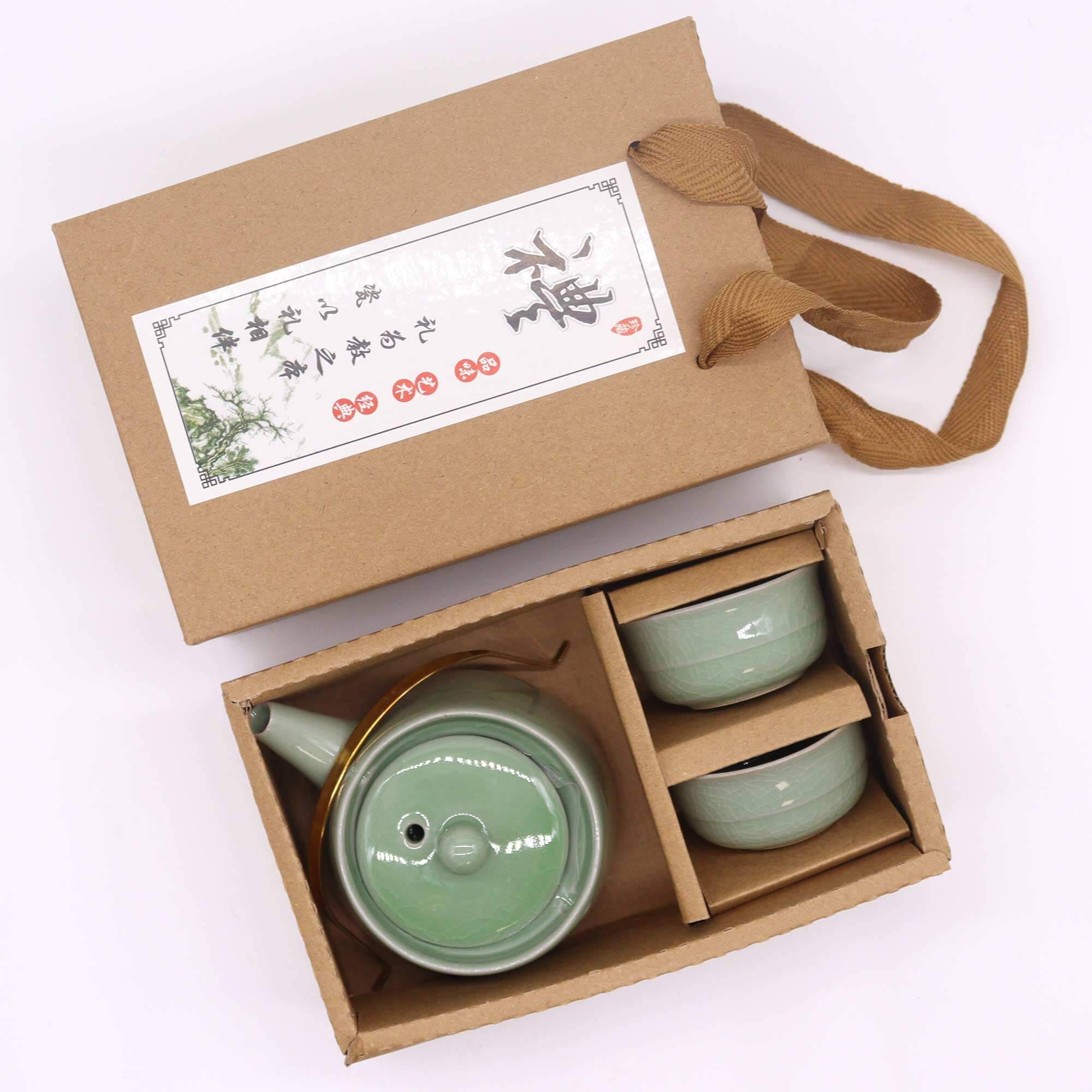 A boxed set containing a green ceramic teapot and two matching cups with a brown handle attached to the packaging.