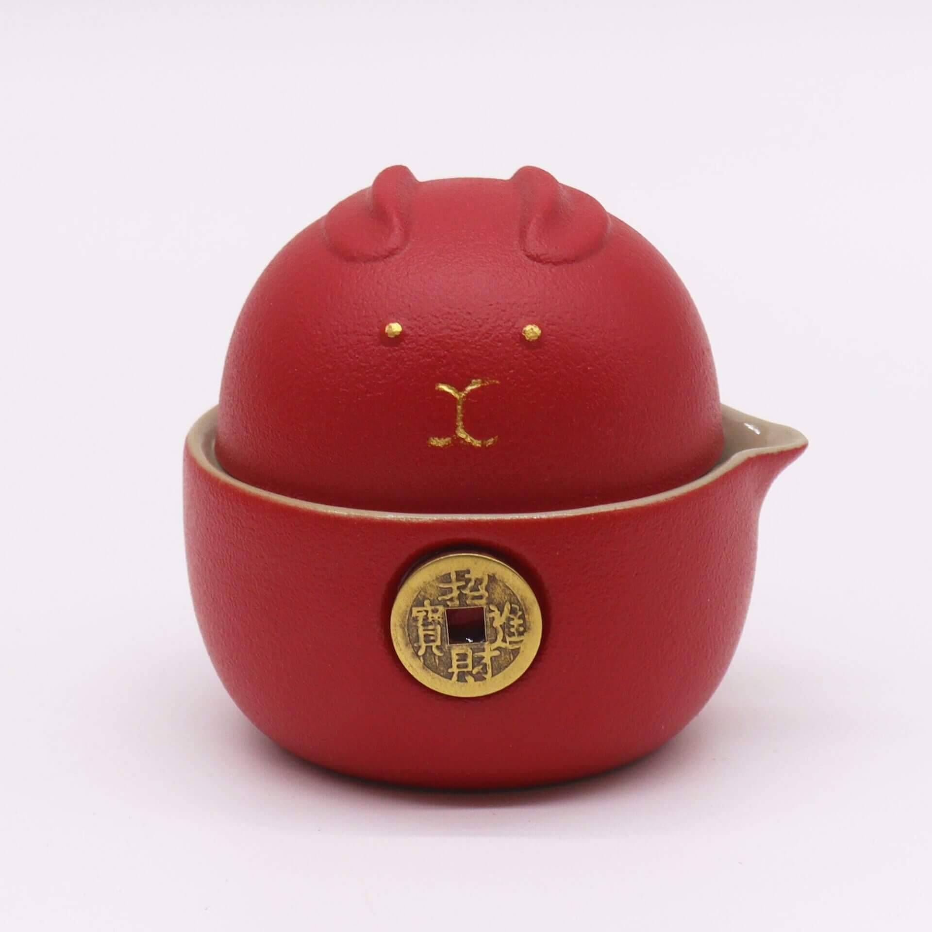 A red ceramic container with a lid shaped like a stylized animal face, featuring gold accents and a gold circular emblem on the front.
