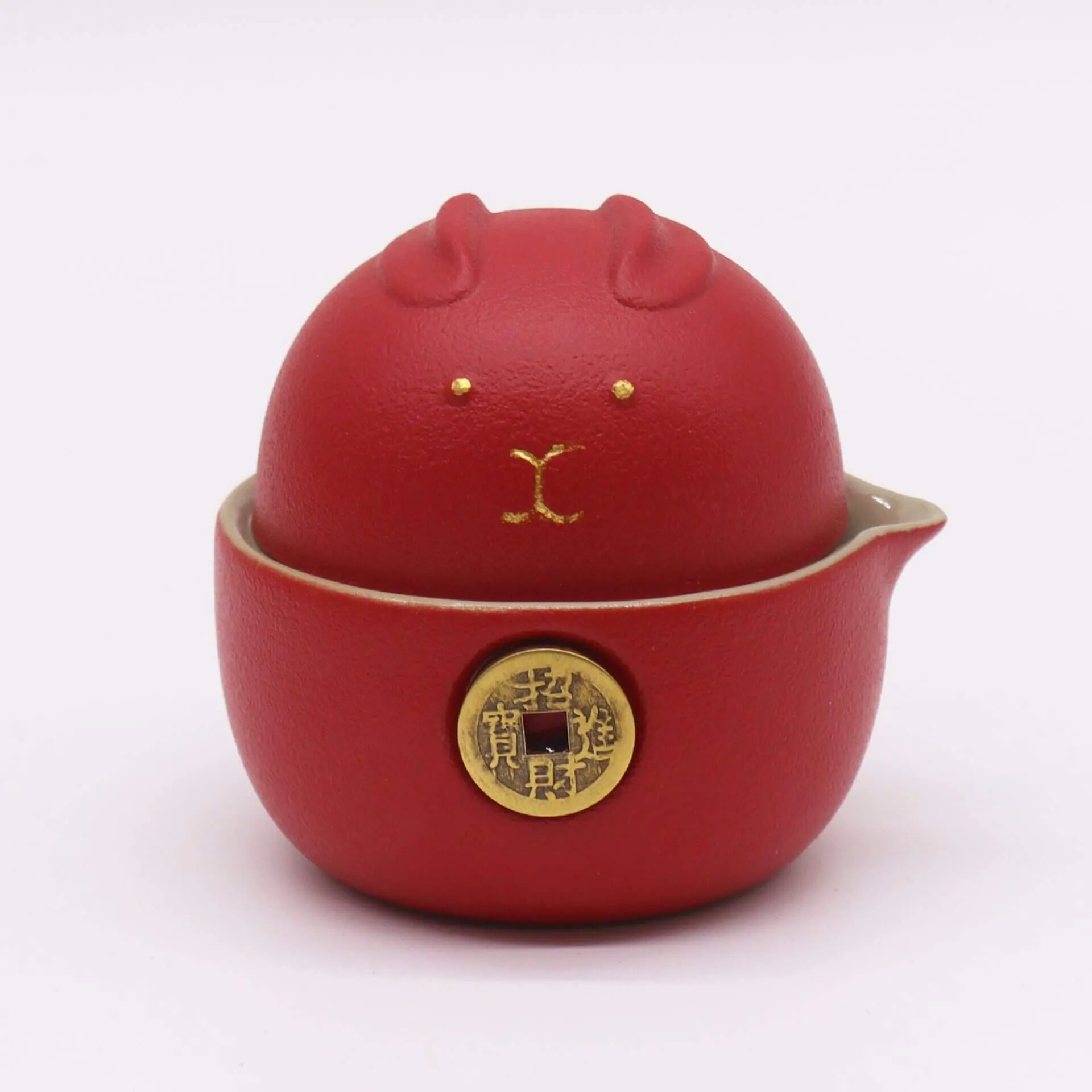 A red ceramic container with a lid shaped like a stylized animal face, featuring gold accents and a gold circular emblem on the front.