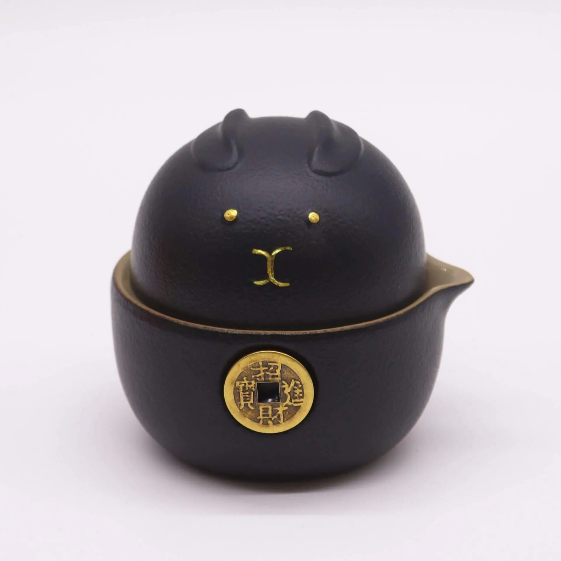 A black, round container shaped like an animal with small ears, gold facial features, and a gold coin design on the front.
