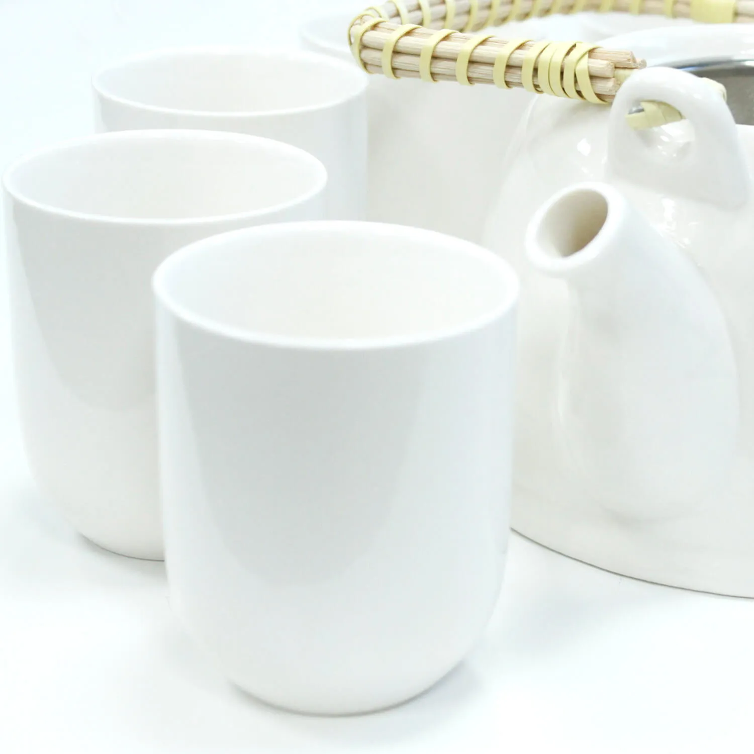 Three white ceramic cups and a white teapot with a woven handle are placed on a white surface.