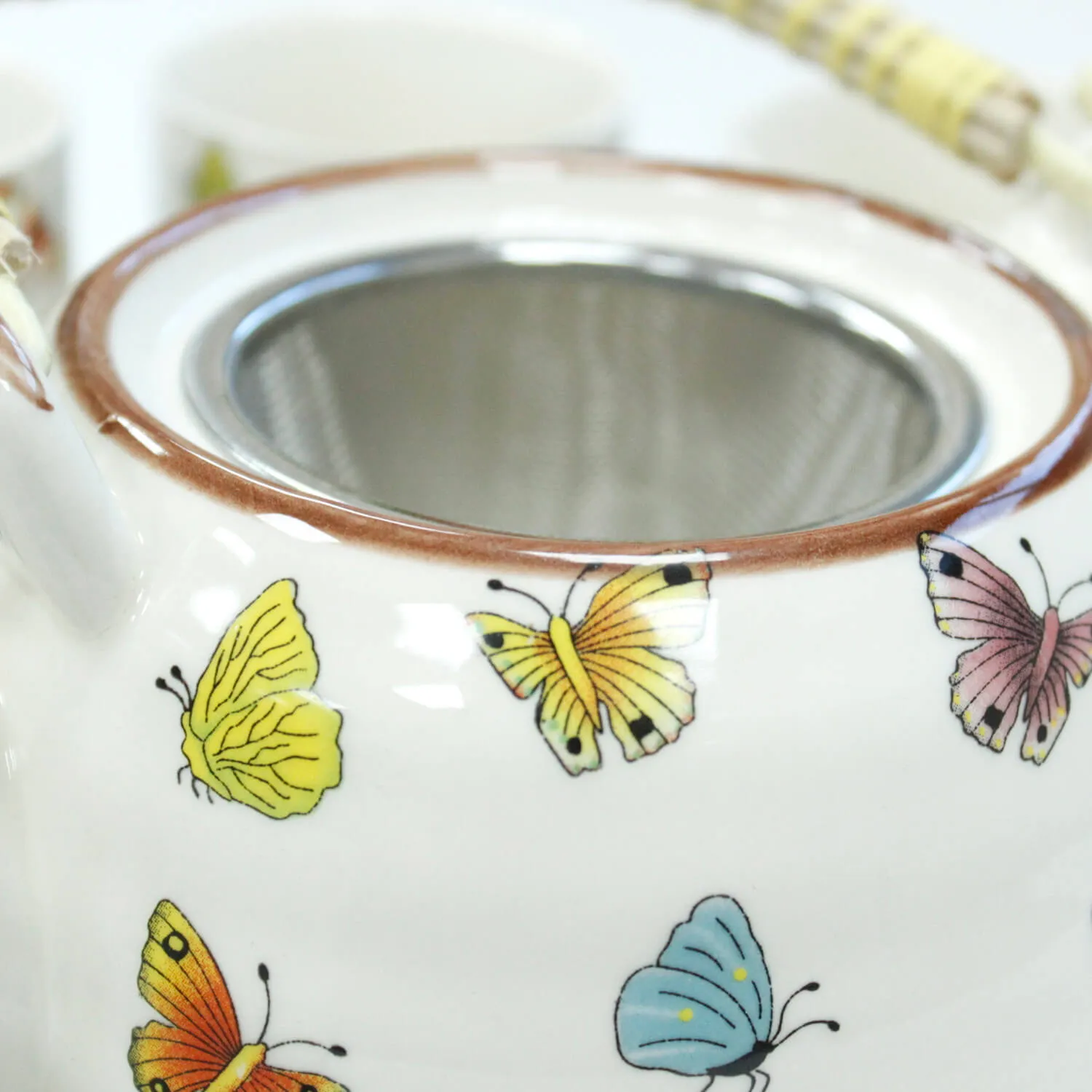 Close-up of a white teapot decorated with colorful butterfly illustrations and a metal mesh strainer inside the opening.