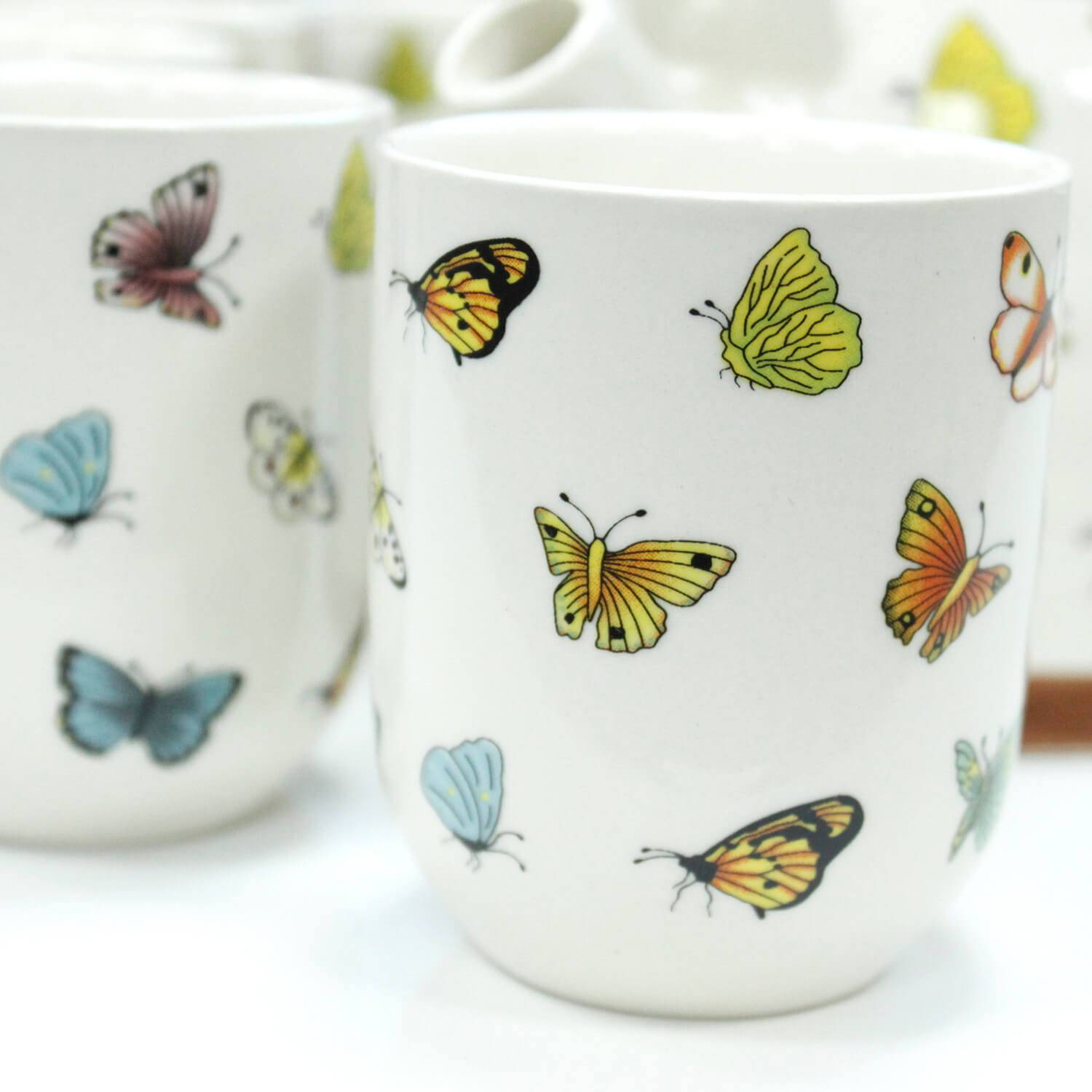 White ceramic mugs decorated with colorful butterfly illustrations in yellow, orange, blue, and pink.