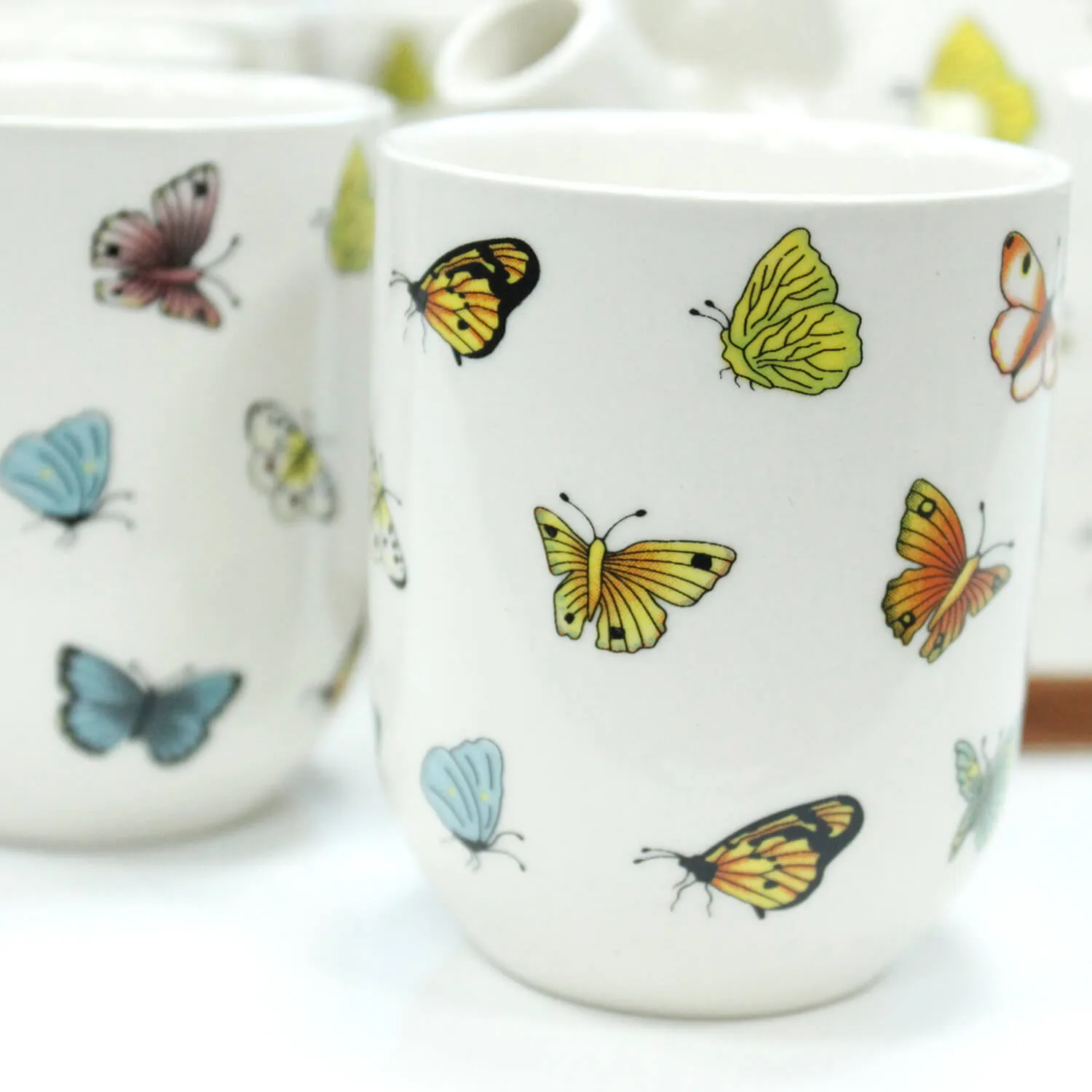 White ceramic mugs decorated with colorful butterfly illustrations in yellow, orange, blue, and pink.