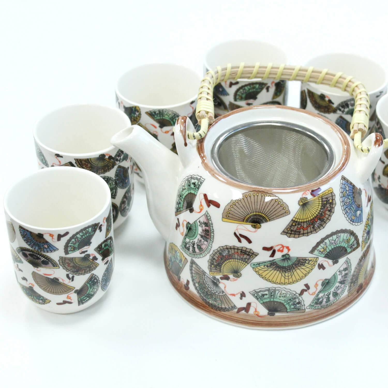 A ceramic teapot with a woven handle and matching cups, all decorated with colorful fan patterns, are arranged on a white surface.