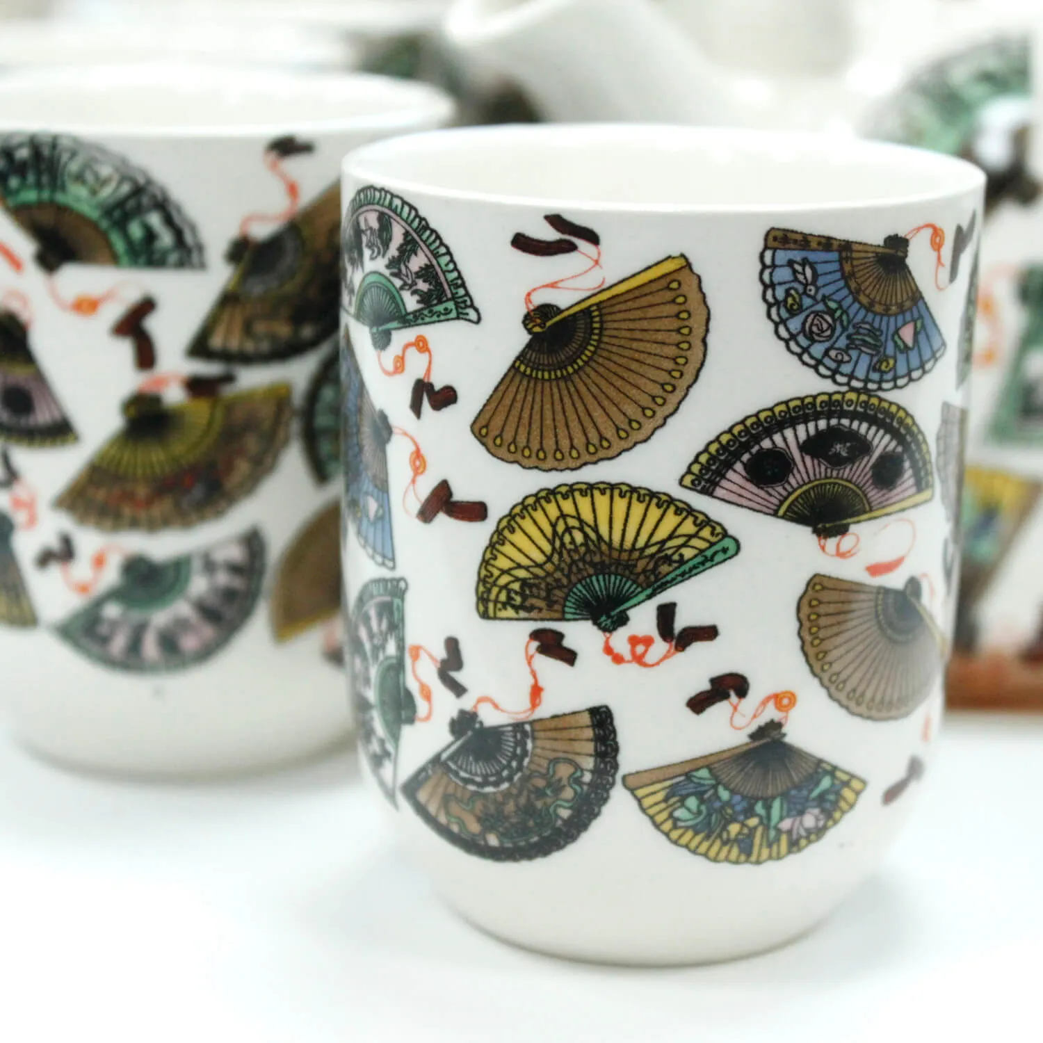 White ceramic cups decorated with colorful, detailed illustrations of folding fans and red ribbons.