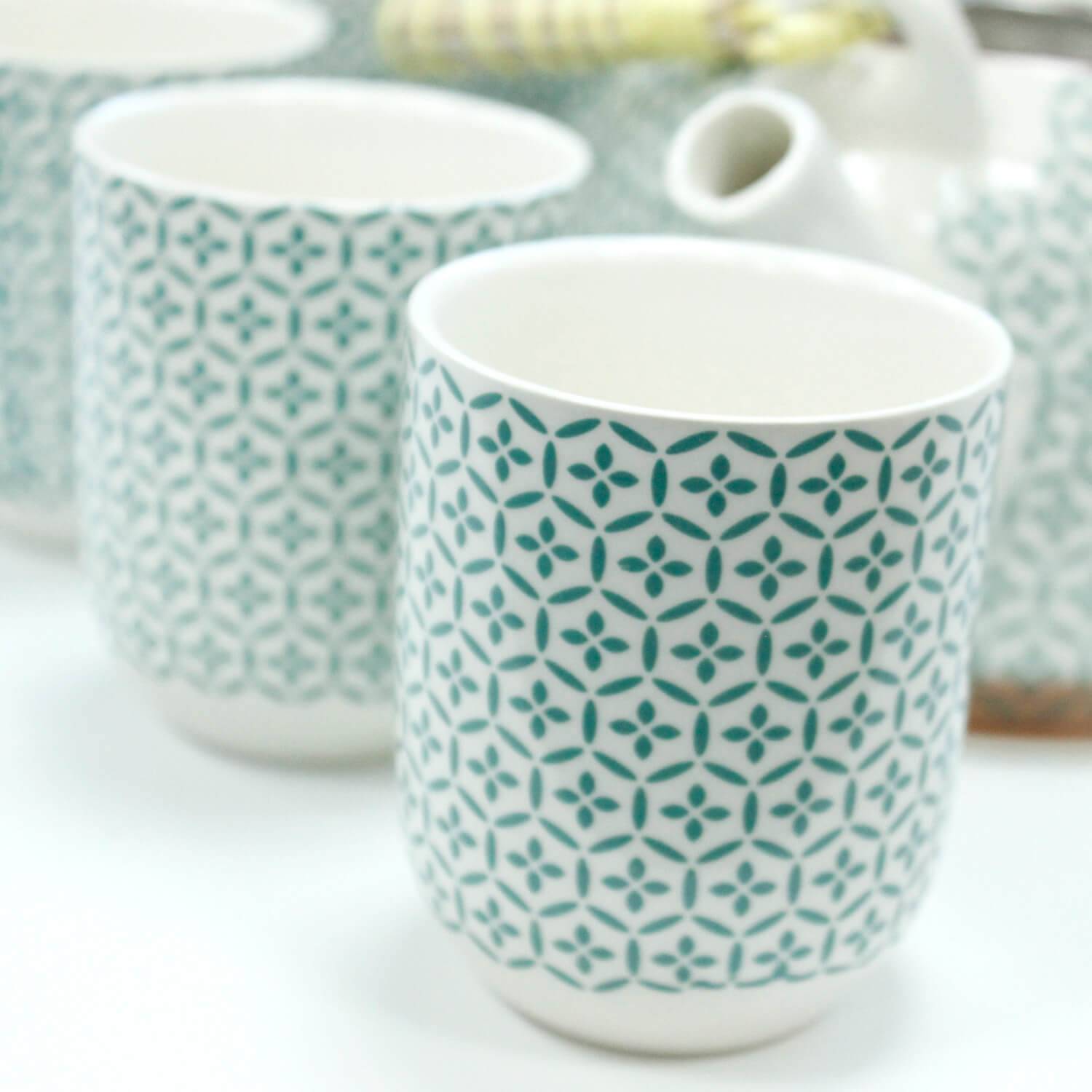 A close-up of patterned ceramic cups with a blue geometric design, arranged on a white surface.