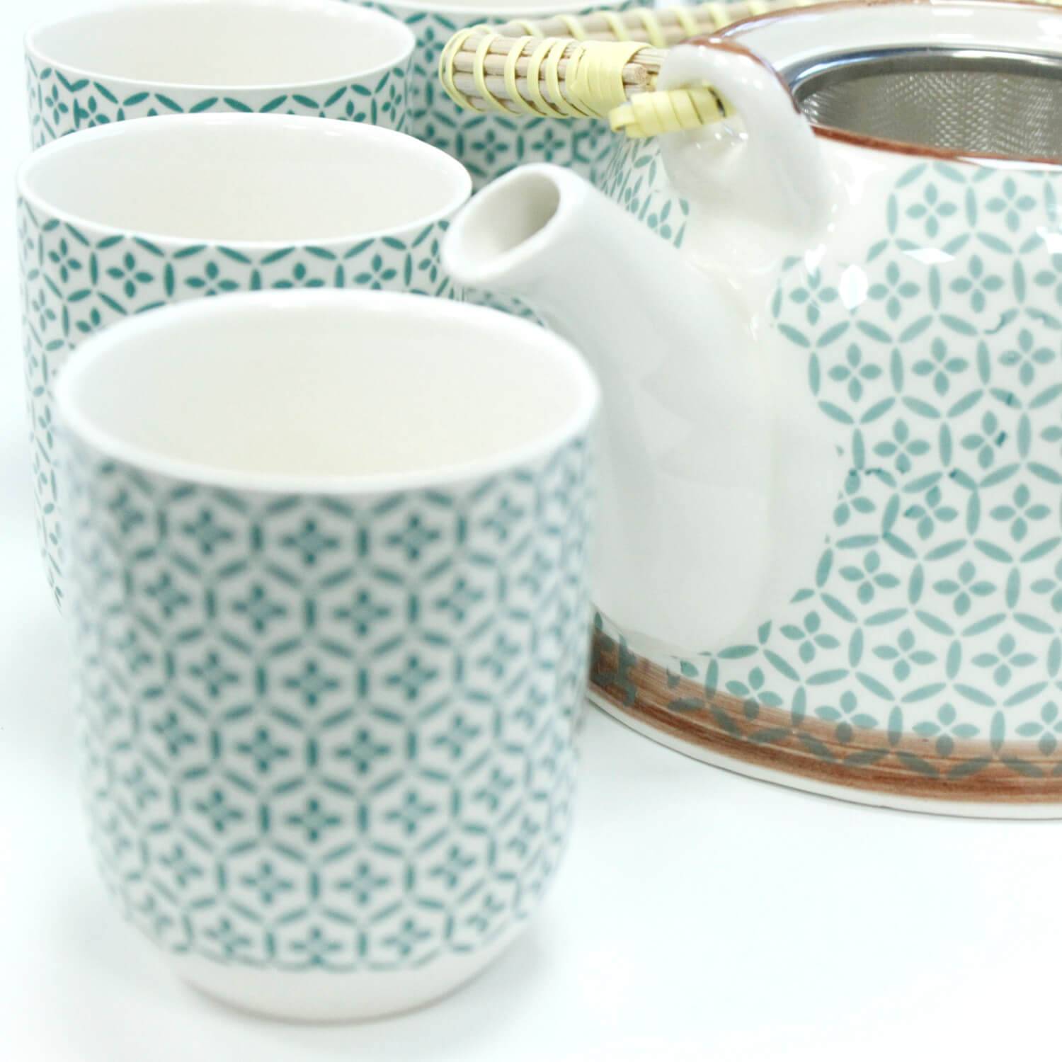 A patterned ceramic teapot with a metal strainer is next to three matching cups, all decorated with a blue geometric design.
