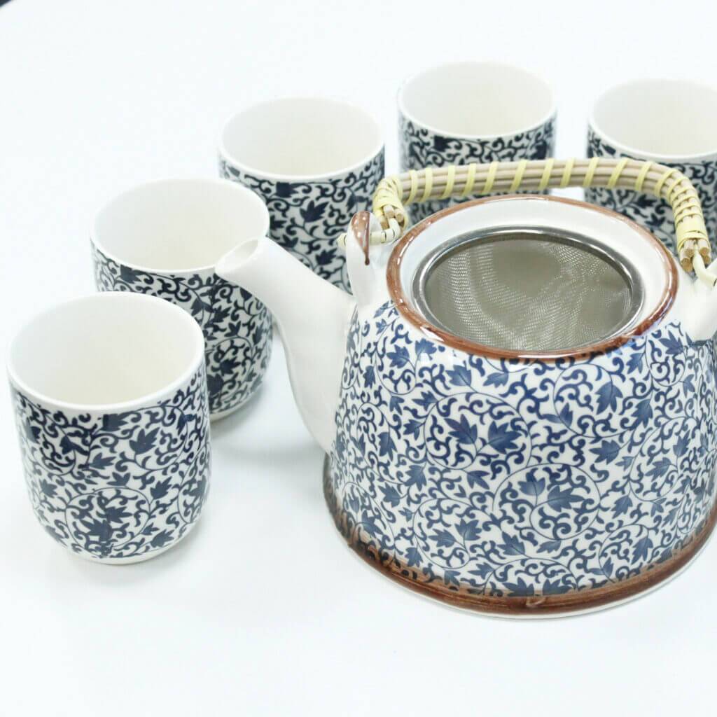 A ceramic teapot with a woven handle and six matching teacups, all featuring a blue and white floral pattern, arranged on a white surface.