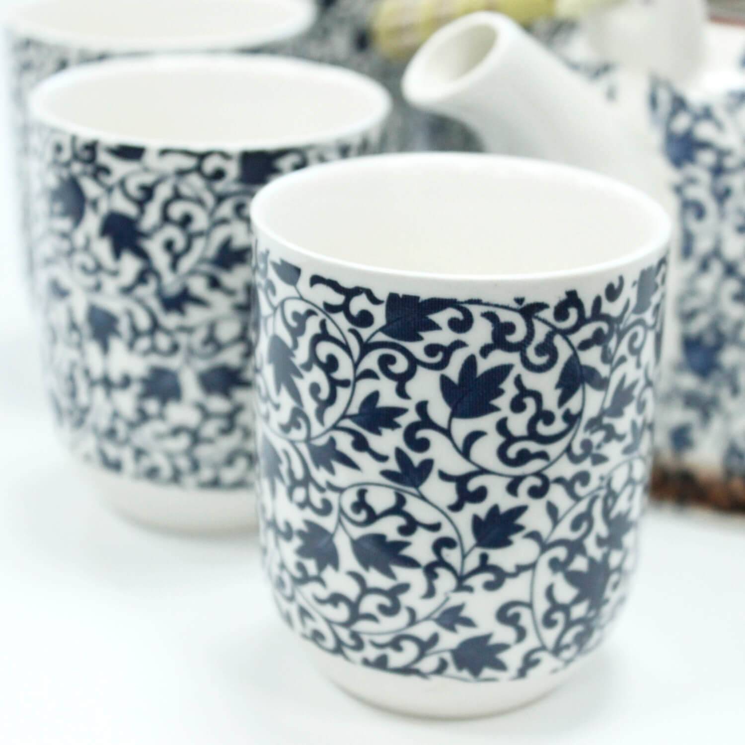 Close-up of white ceramic cups with intricate dark blue floral patterns, accompanied by a matching teapot in the background.