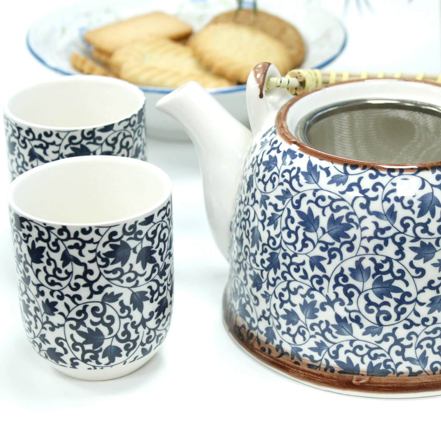 A teapot and two matching cups with blue floral patterns are set beside a plate of rectangular biscuits.