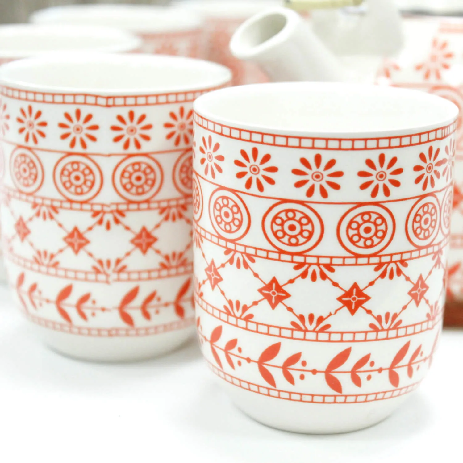 White ceramic cups with red geometric and floral patterns, grouped together on a white surface.
