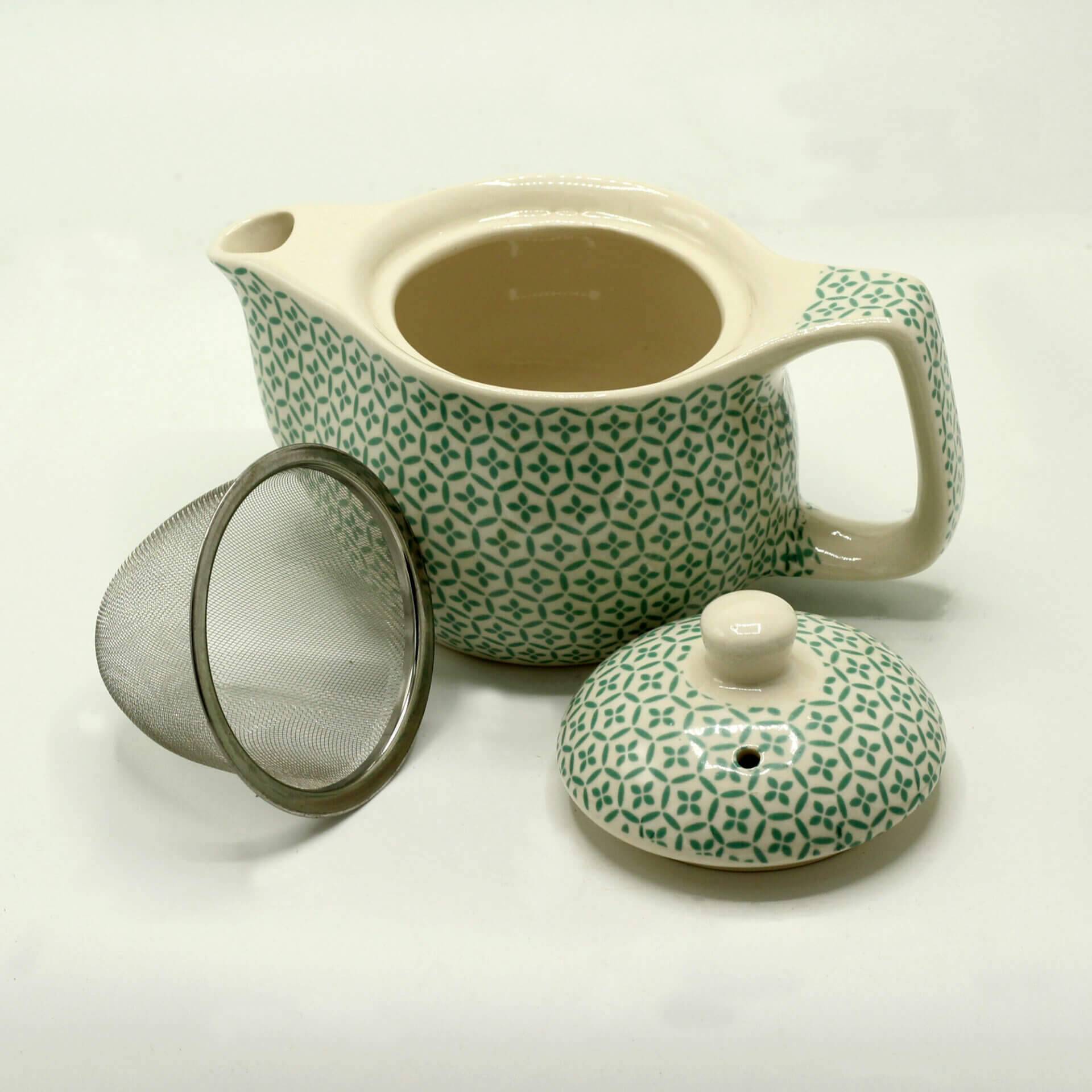 A ceramic teapot with a green geometric pattern, shown with its lid removed and a metal mesh infuser placed beside it, against a plain background.