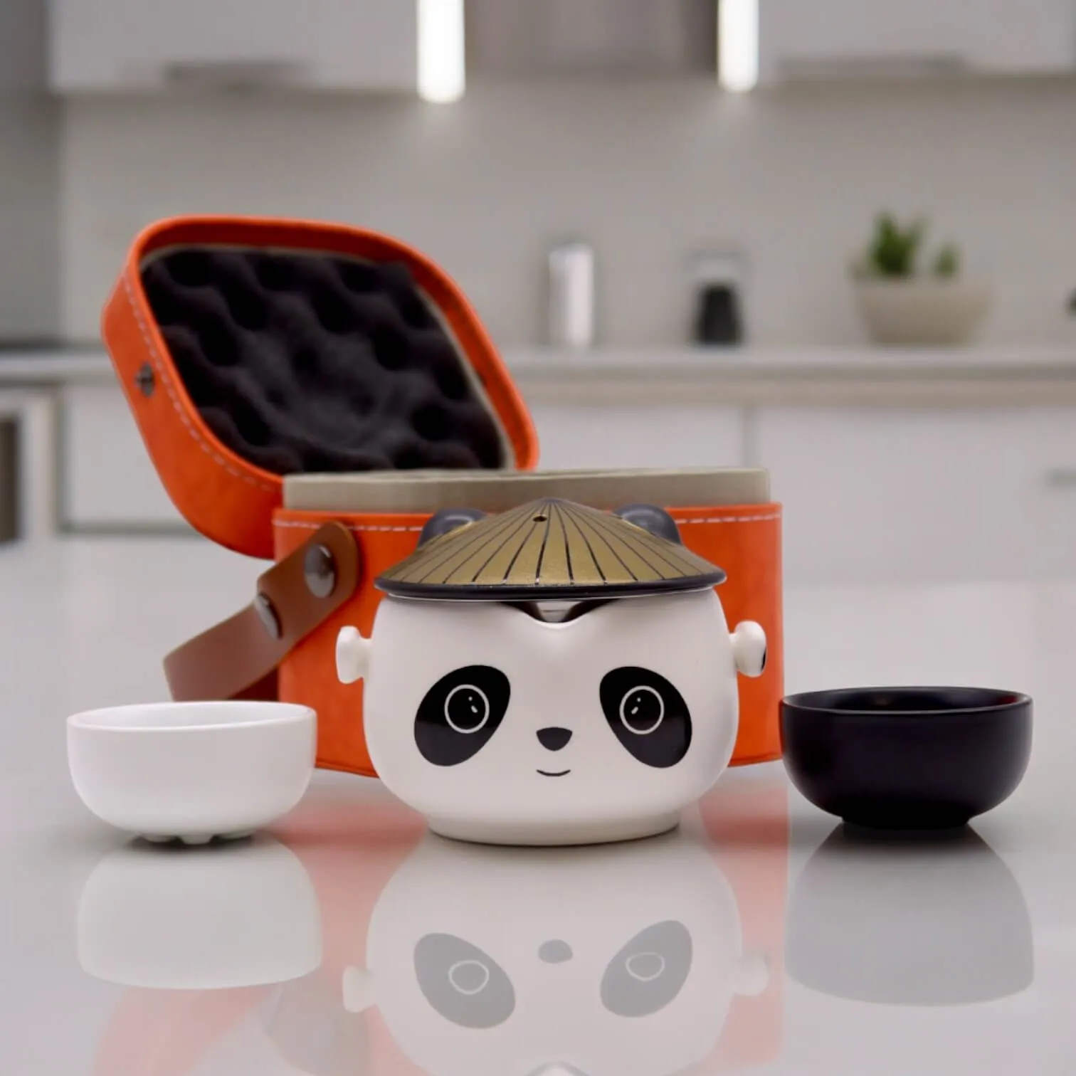 A panda-shaped tea set with two small cups and an orange carrying case is displayed on a kitchen countertop.