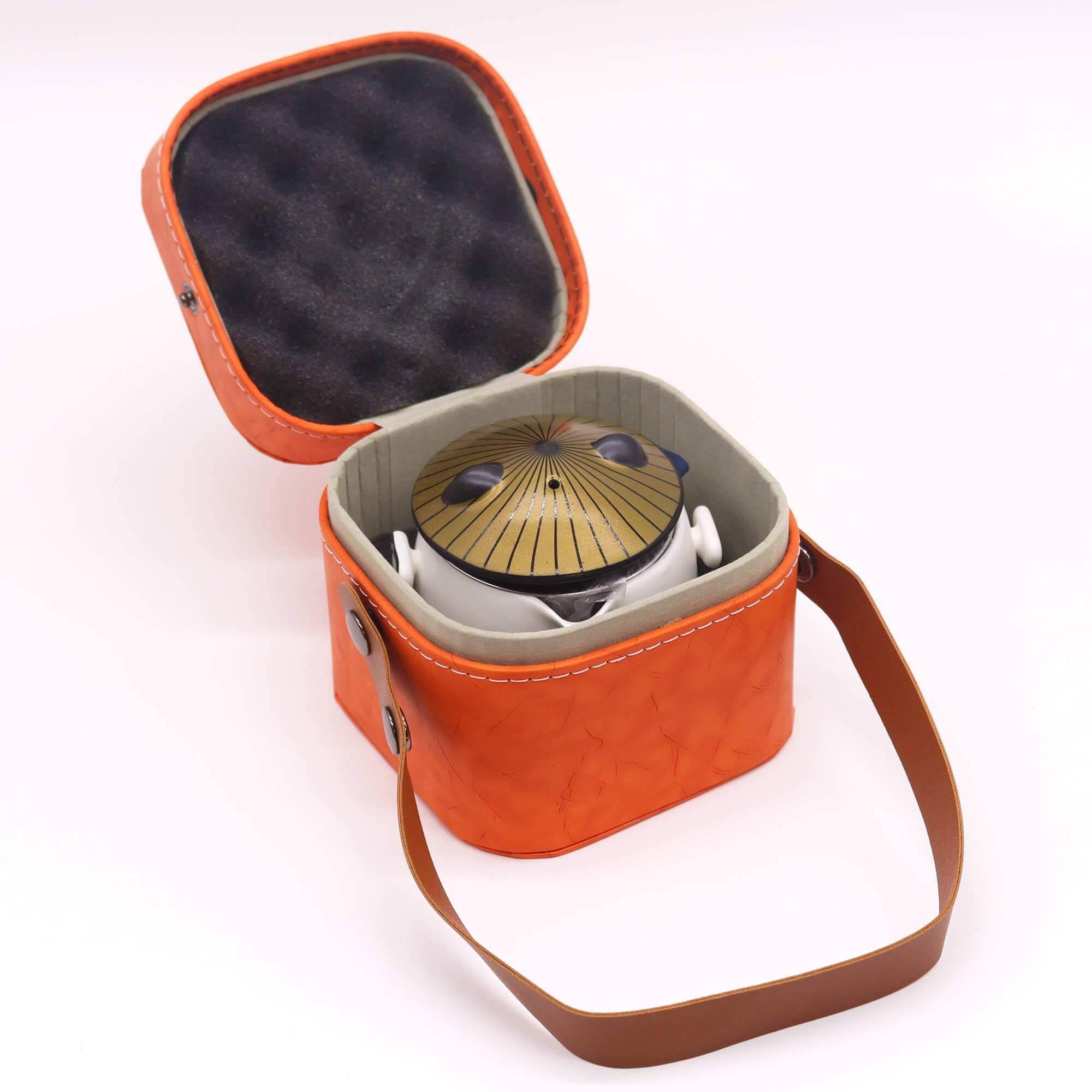 A small steel tongue drum in an orange carrying case with a brown strap and gray interior, shown on a white background.