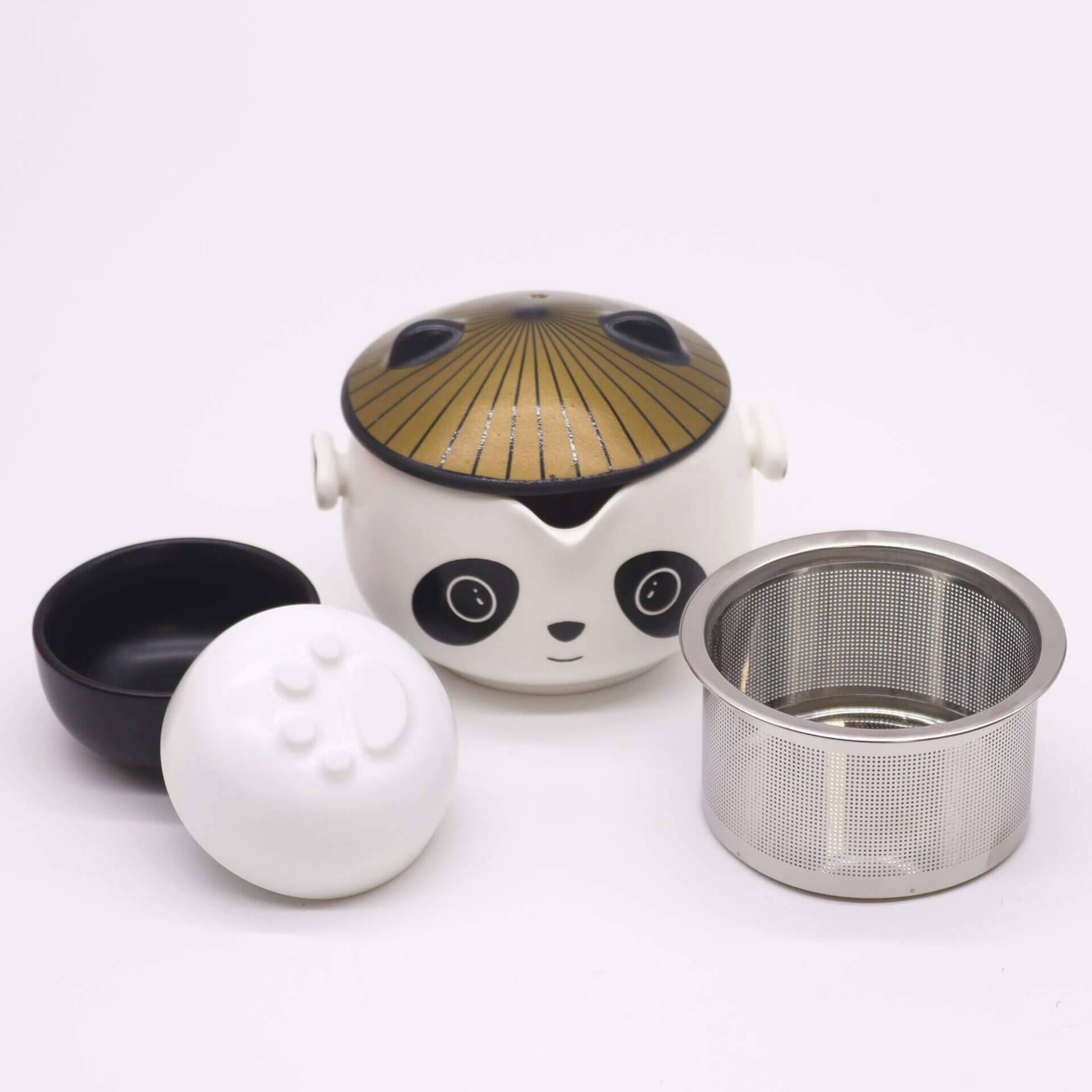 A panda-shaped teapot with a gold lid, a black bowl, a white lid, and a metal tea infuser are displayed on a white background.