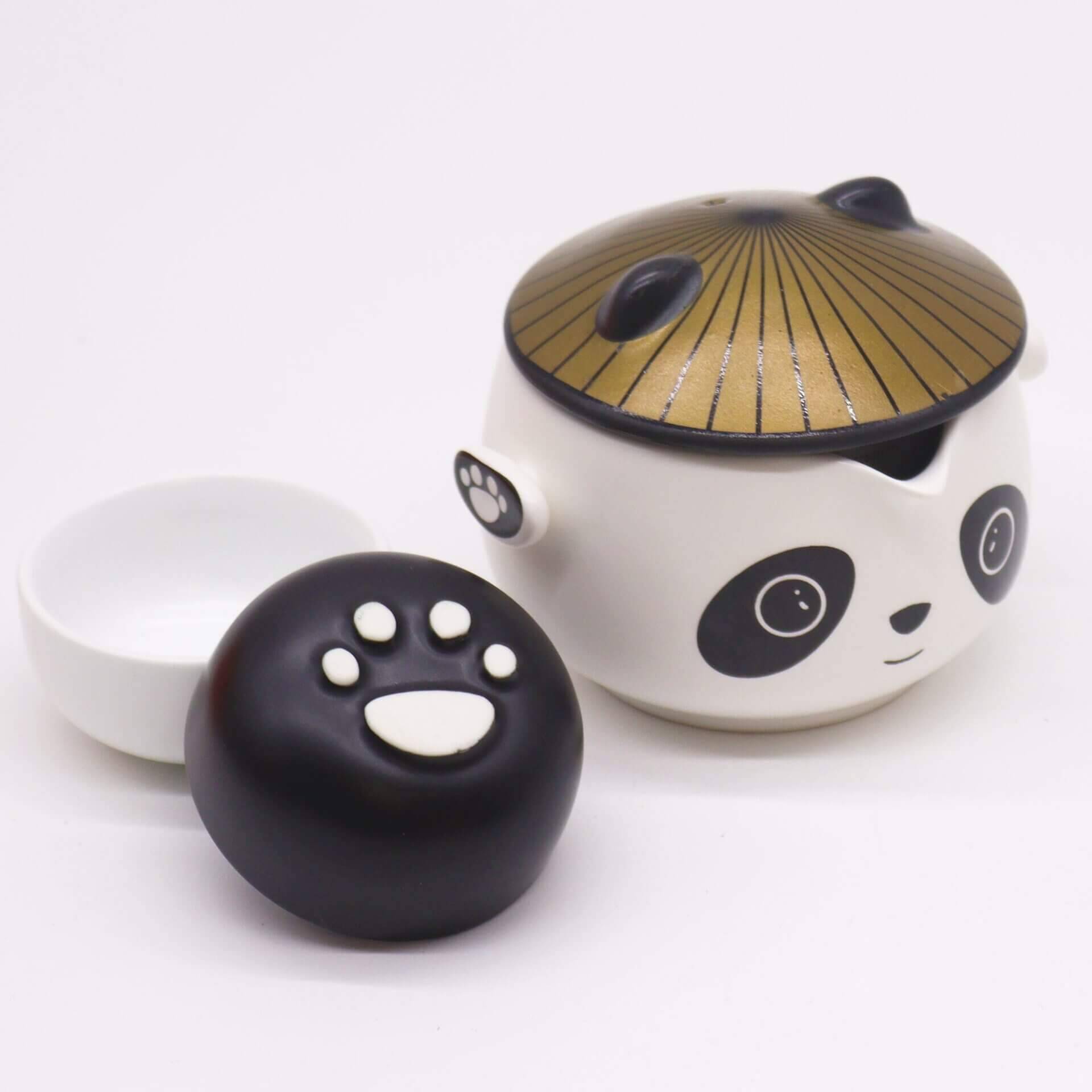A ceramic teapot shaped like a panda, with a gold lid, a black paw-shaped lid, and a small white cup, all on a plain white background.