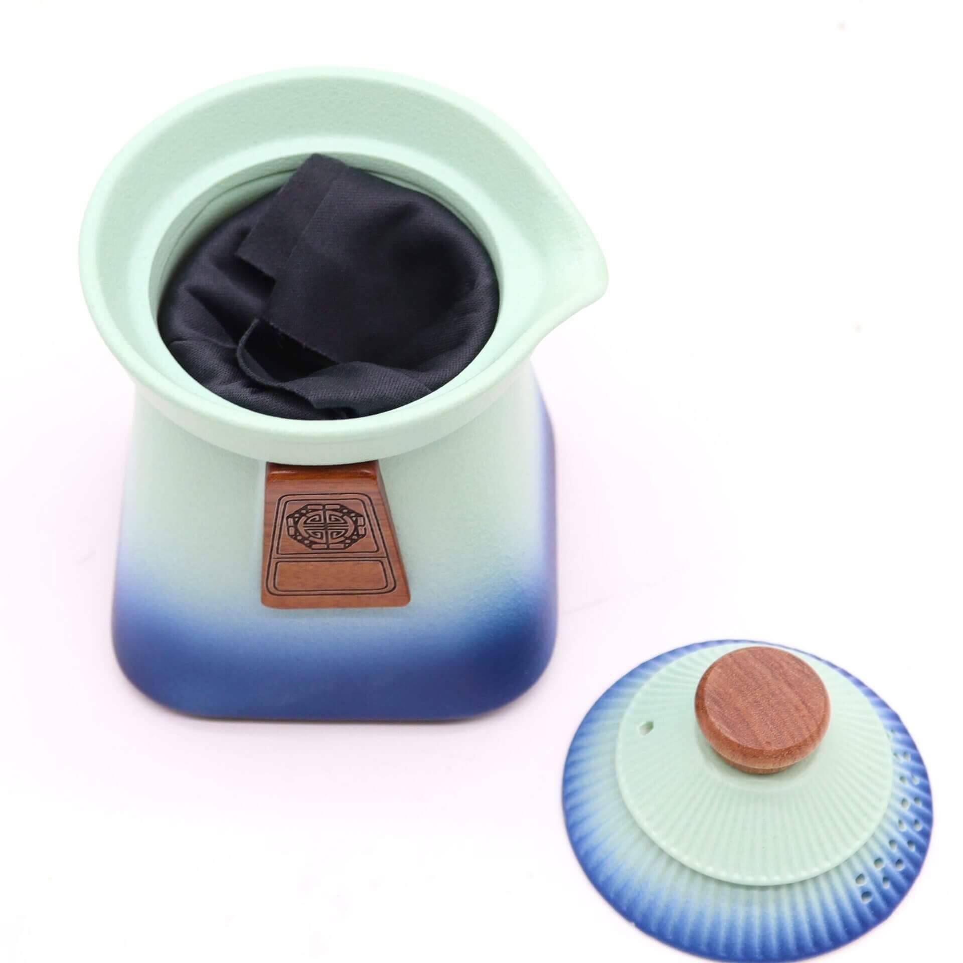 A ceramic container with a wooden emblem holds a black cloth; its matching blue and wooden lid is placed beside it on a white background.