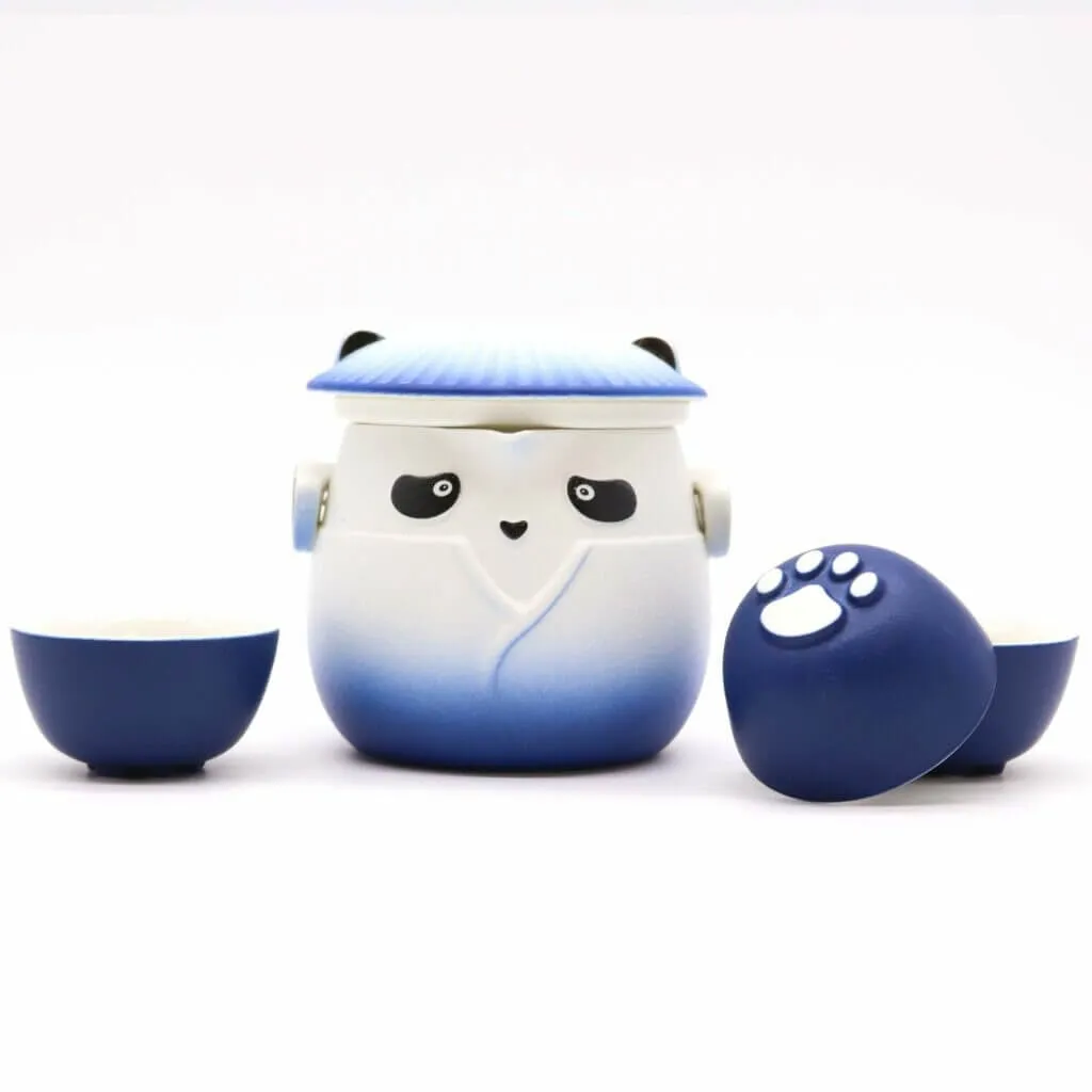 A blue and white panda-shaped teapot with a lid, flanked by two matching teacups, one turned to show a white paw print on its base.