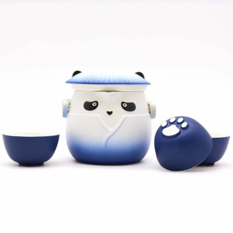 A blue and white panda-shaped teapot with a lid, flanked by two matching teacups, one turned to show a white paw print on its base.