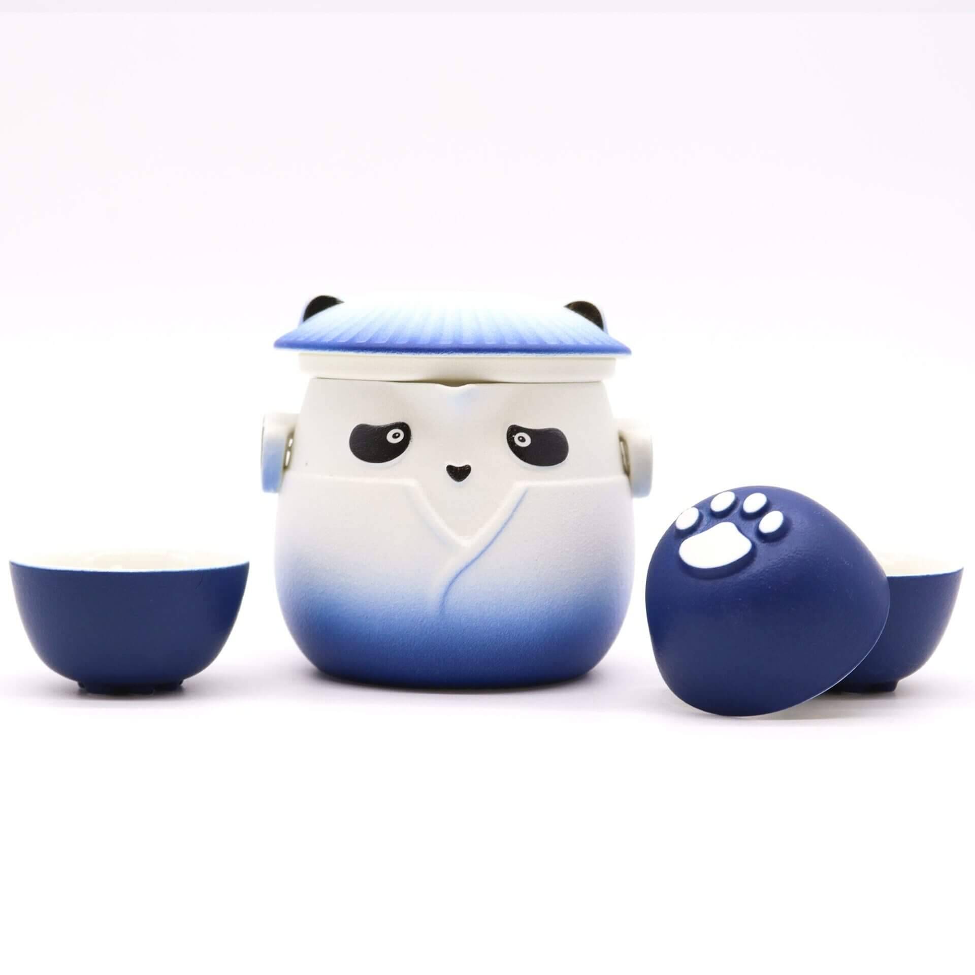 A blue and white panda-shaped teapot with a lid, flanked by two matching teacups, one turned to show a white paw print on its base.