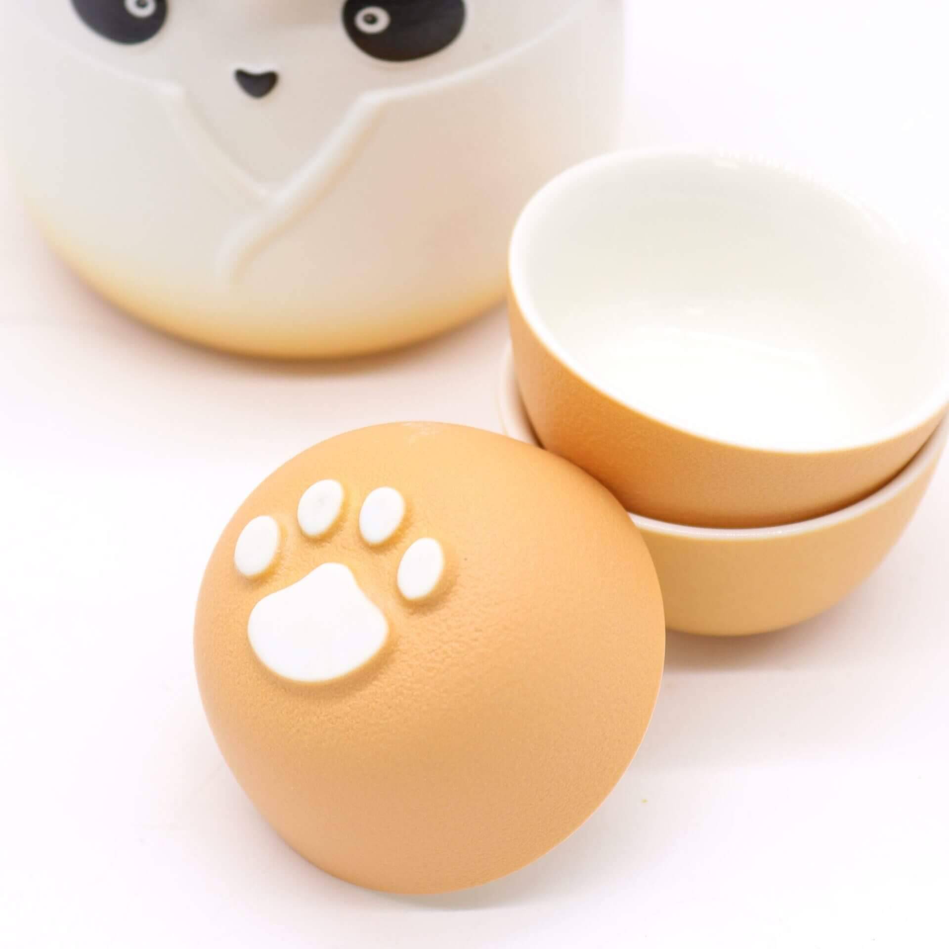 Two small ceramic bowls are stacked next to another bowl showing its base, which features a white paw print design. Part of a larger container with a panda face is also visible.