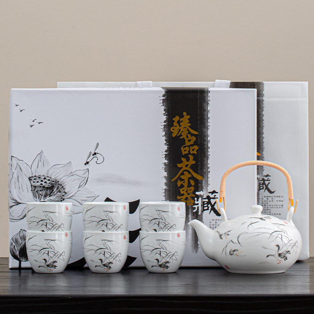A white porcelain tea set with a teapot and six cups featuring black floral designs, displayed in front of decorative packaging with Chinese characters.