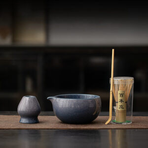 The Kiln-Glazed Matcha Set – 4 Piece | Stone includes a ceramic small pitcher, bowl, bamboo whisk, and scoop on a mat, adding elegance to your tea ritual.