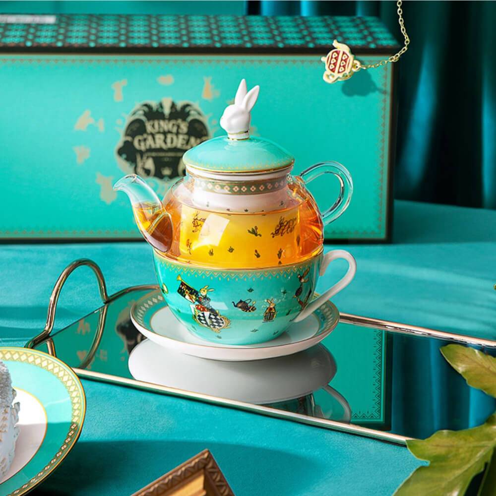 The Alice in Wonderland Inspired Rabbit Teapot Set from the Luxury Afternoon Tea Collection features a charming teal teapot with a rabbit-shaped lid, matching teacup, and a "King's Garden" green box backdrop for an enchanting tea experience.