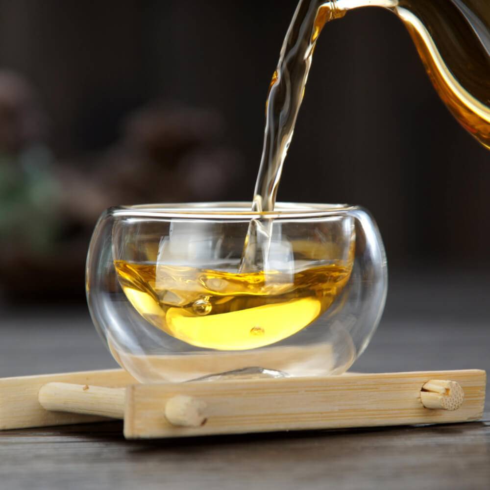 Tea is poured into the Professional Tea Master's Double-Wall Cup, an exquisite insulated tasting vessel, elegantly resting on a small wooden tray.