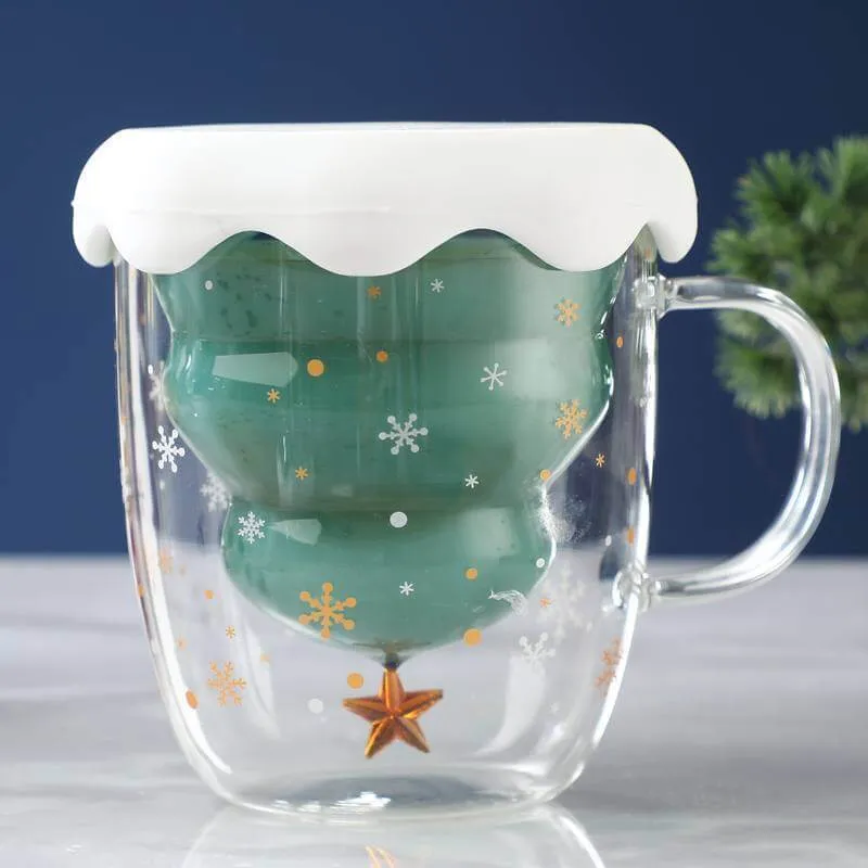 Clear glass mug with a green, inverted Christmas tree inside. The mug has a white lid resembling snow and features snowflake designs.